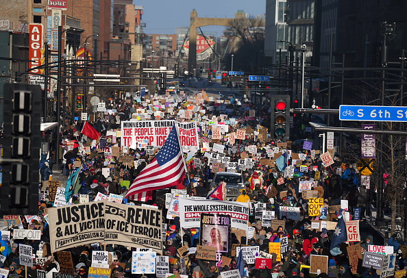 Mmarchers in downtown Minneapolis wave signs decrying ongoing immigration enforcement operations...