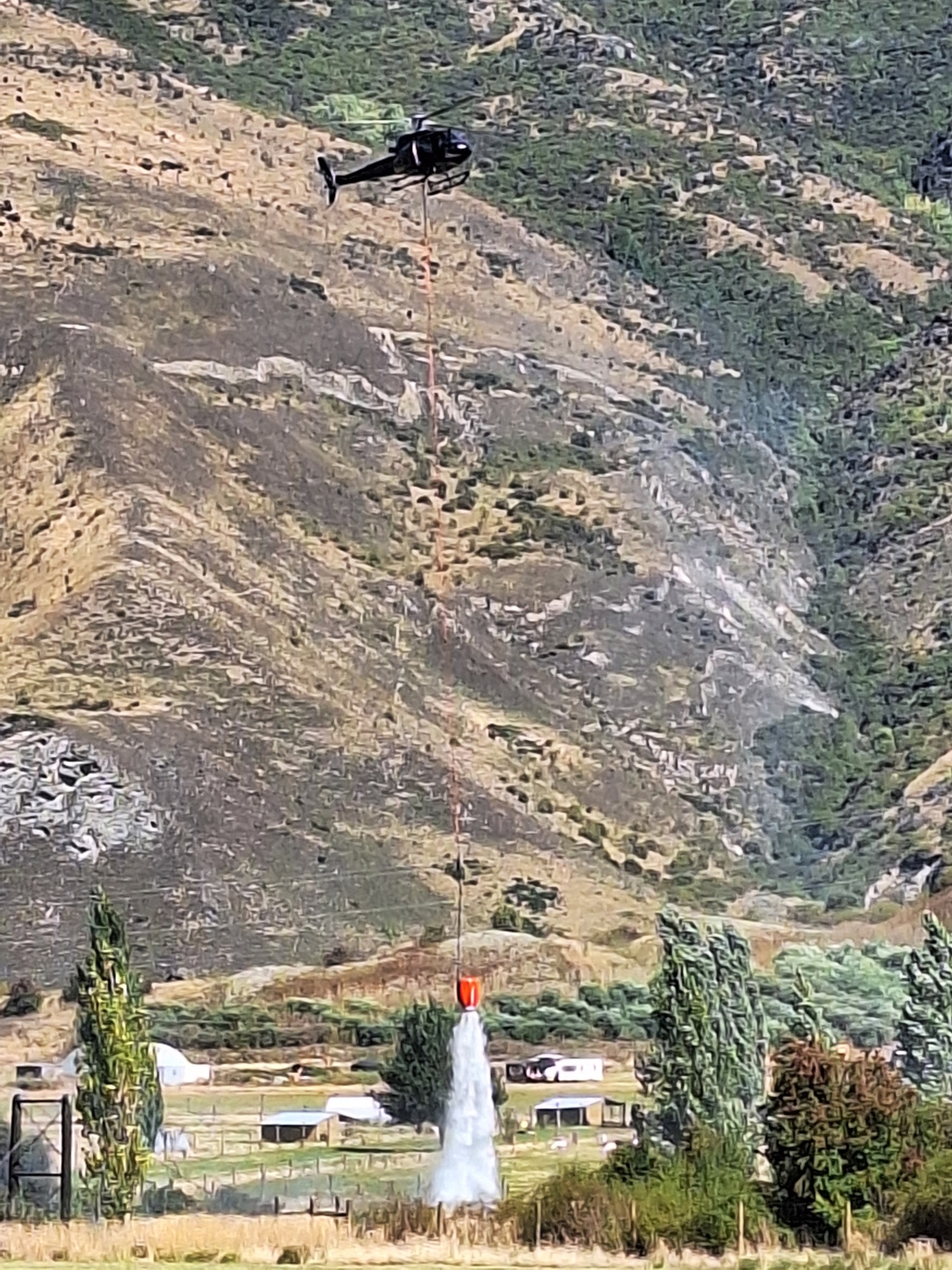 A helicopter with a monsoon bucket dumps water on the blaze. Photo: Guy Williams 