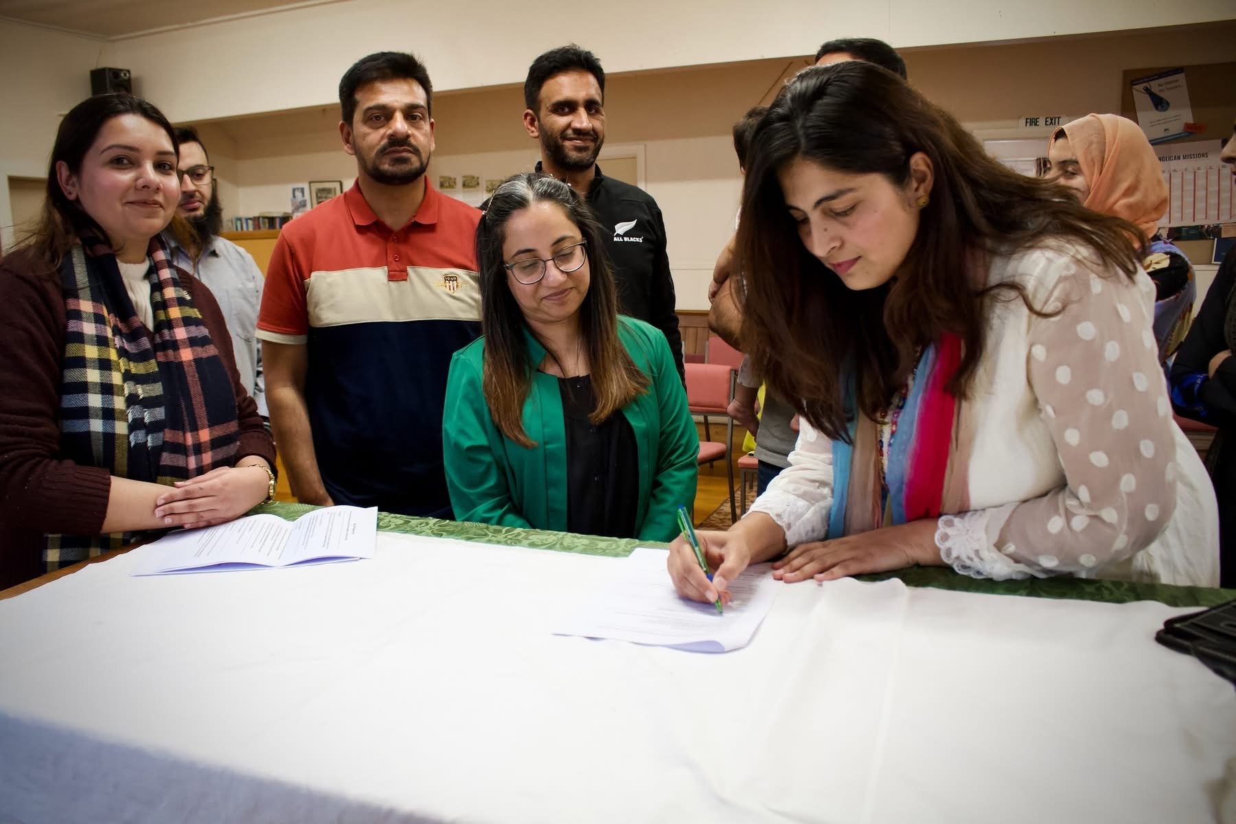 Pakistani Community of Otago president Anam Nawaz signs documents formalising the merger of the...