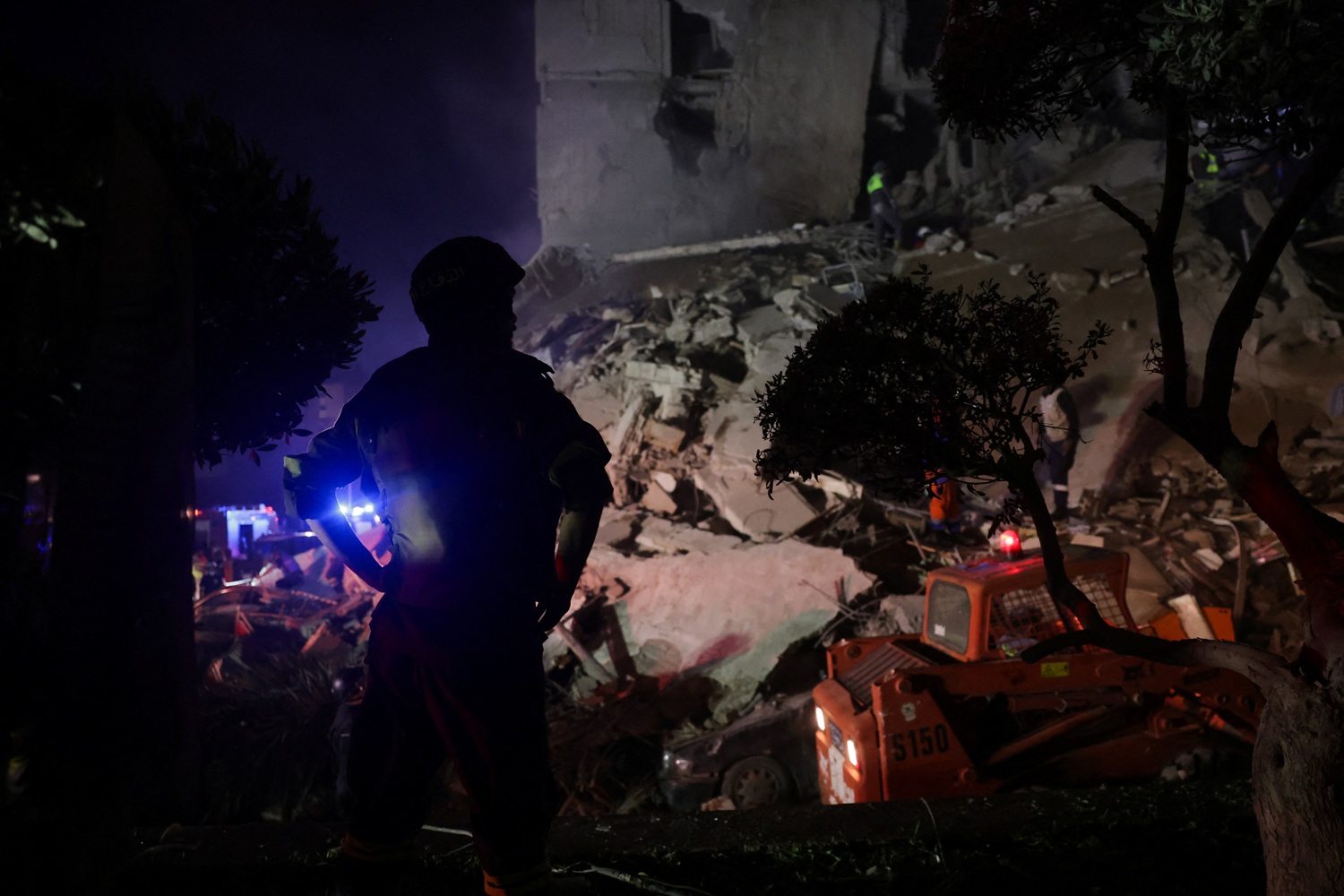 A rescuer looks on as others save people from a damaged building following an Israeli strike in...