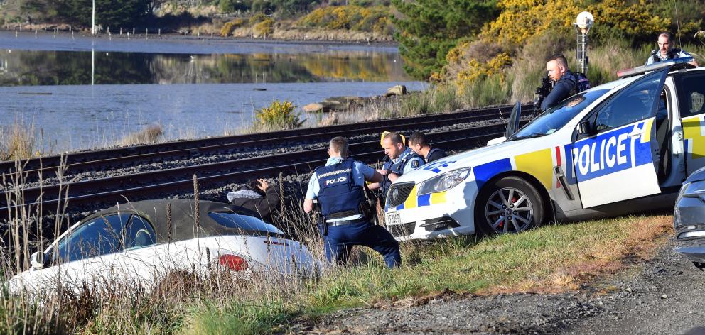 Police lower their weapons after a man gets out of a Volkswagen which crashed on to the railway...