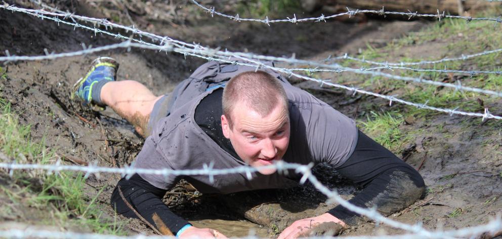 Balclutha man James McDonald crawls cautiously  under barbed wire at  the Balclutha Mud Trudge on...