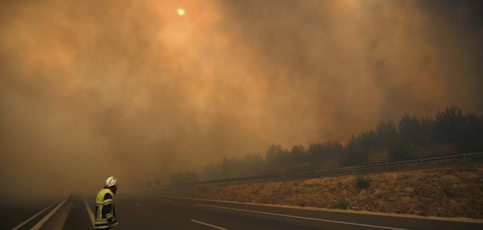 A French fireman stands in the road as smoke fills the sky and partially blocks the sun as fires...