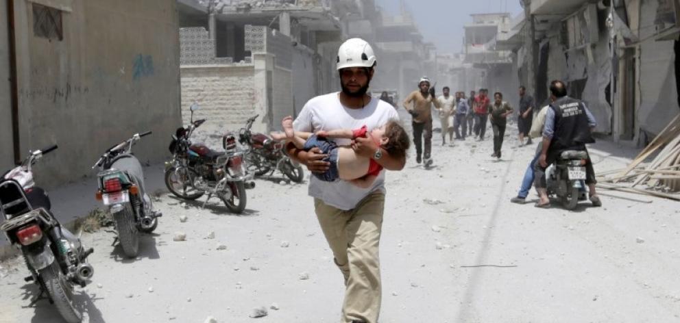A civil defence member carries an injured girl at a site hit by airstrikes in the rebel...