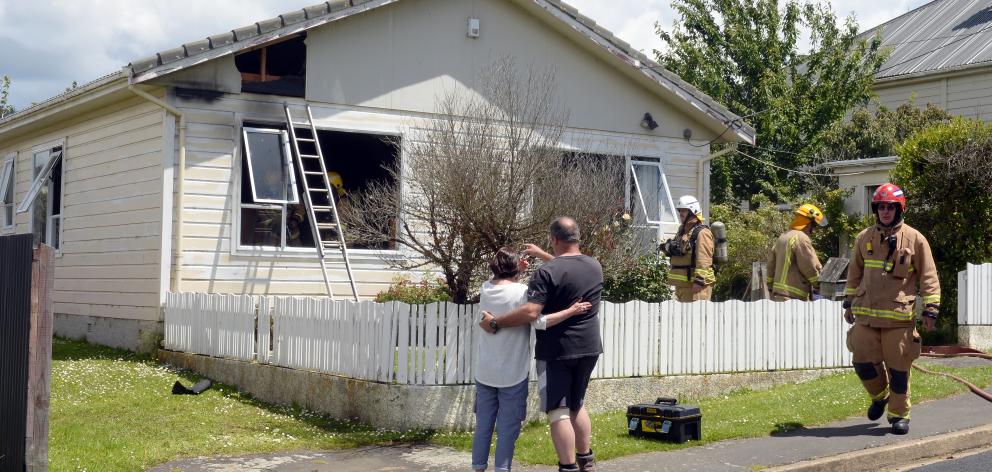 Steve Wedlock is comforted by a woman as firefighters work in his Sawyers Bay home yesterday....