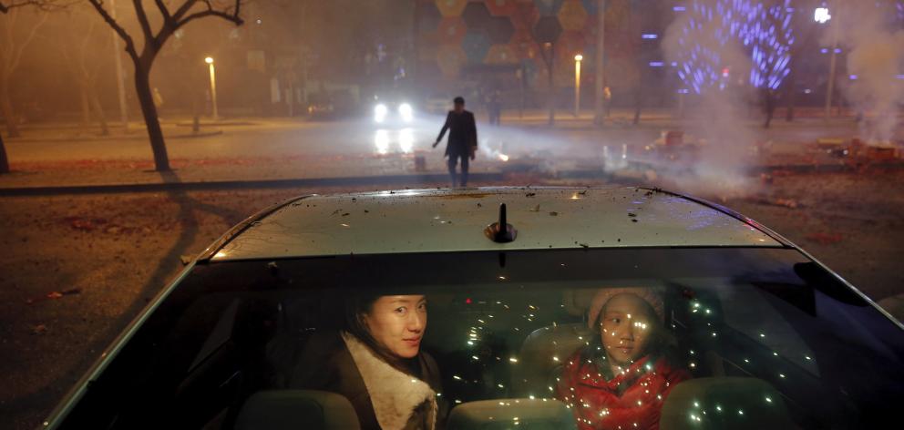 A girl and a woman sit inside the car as firecrackers and fireworks explode celebrating the start...