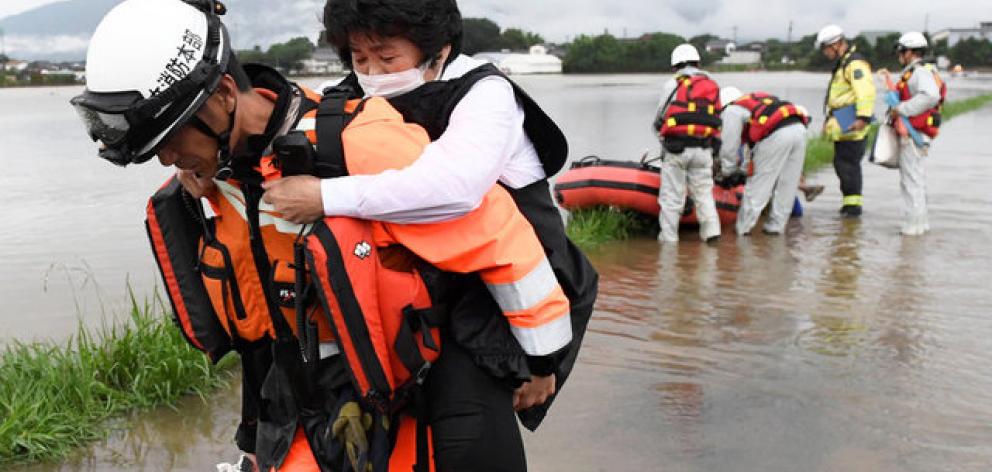 Local resident is rescued by a firefighter after heavy rain hit the area in Asakura. Photo: Reuters