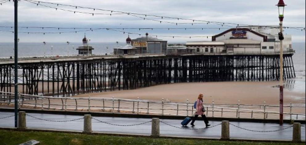 A woman pulls her suitcase past the North Pier in Blackpool, Britain. Photo: Reuters