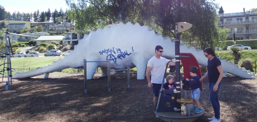 Tourists Scott and Hannah Walmsley and their children Nina (16 months) and Ryan (2) in front of the vandalised  dinosaur in the children’s playground on Saturday. Photo: Kerrie Waterworth