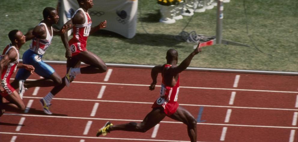 Canadian Ben Johnson celebrates as he crosses the finish line ahead of American Carl Lewis and...