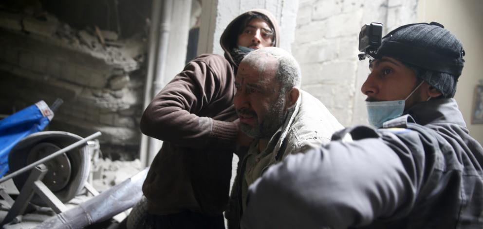 Civil defence personnel help a man from a shelter in the besieged town of Douma in eastern Ghouta...