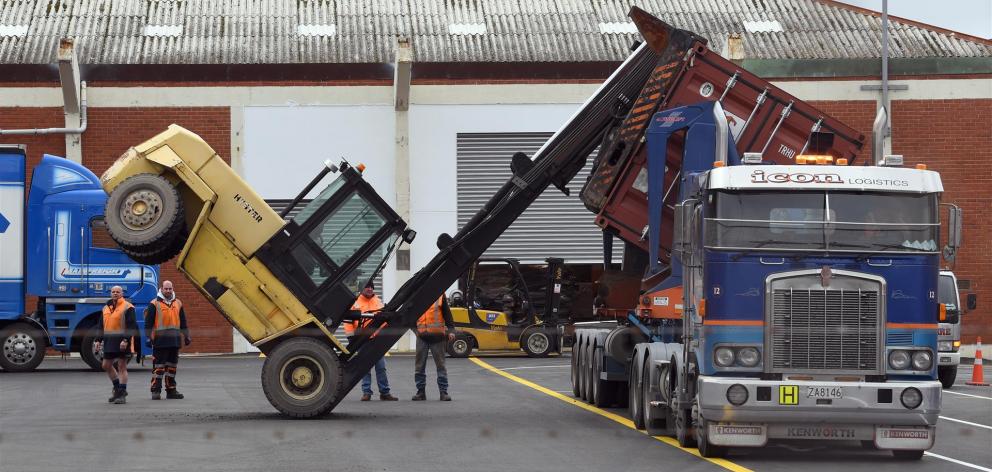 Workers consider what to do next after a forklift tipped forward while lifting a container in a...