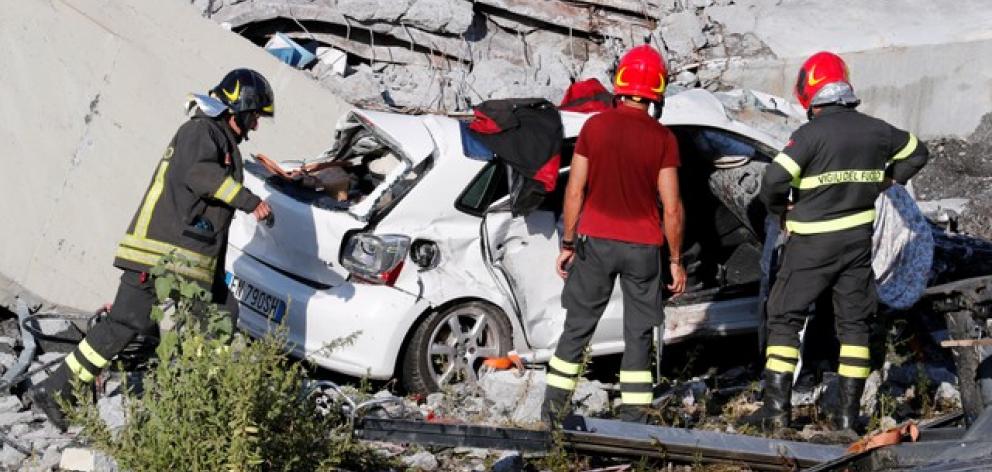 Firefighters stand inspect crushed car at collapsed Morandi Bridge site in Genoa. Photo: Reuters