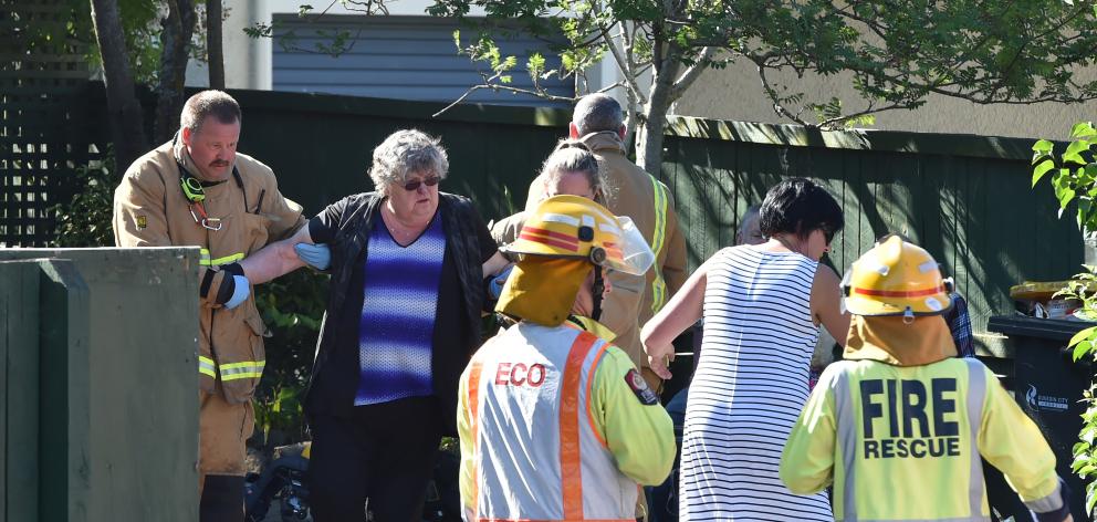 Firefighters help a woman to a waiting ambulance after a fire at Dunedin home yesterday afternoon. Photo: Gregor Richardson