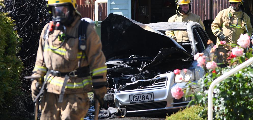 Firefighters inspect the wreckage of a car in Mosgiel which burst into flames yesterday morning....