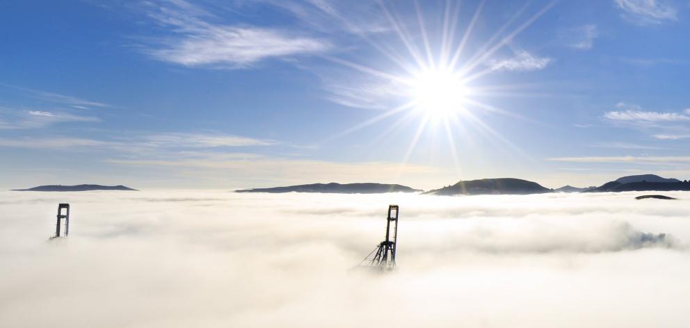 Port Otago container cranes poke through thick fog at Port Chalmers yesterday morning, as the sun rises over the peaks of the Otago Peninsula in the background. Photo: Stephen Jaquiery