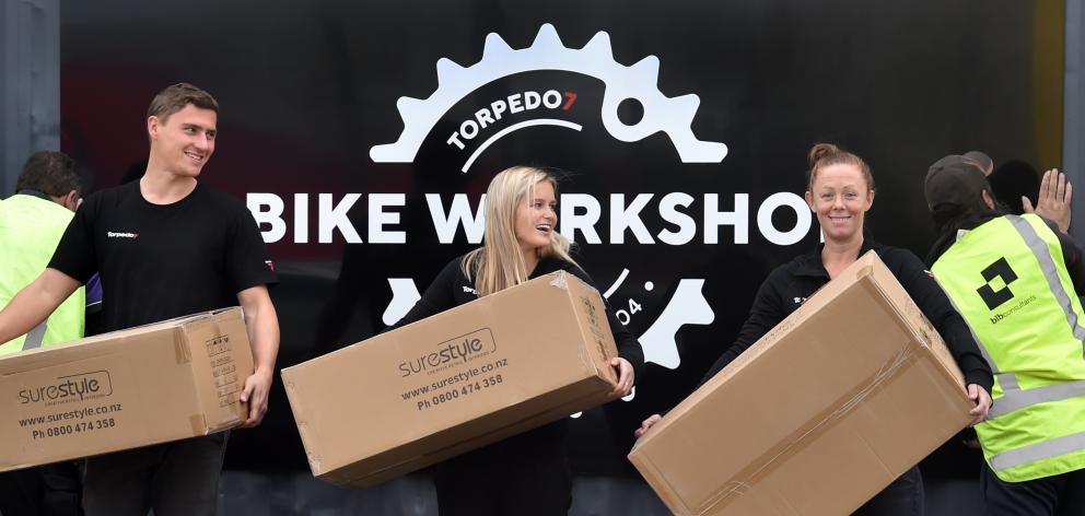 Torpedo7 staff at the Andersons Bay Rd outlet (from left) bike mechanic Sebastien Bossard and sales team members Sophie Letcher and Carole McCaughan move goods while, in the background, workmen affix new signs. Photo: Peter McIntosh