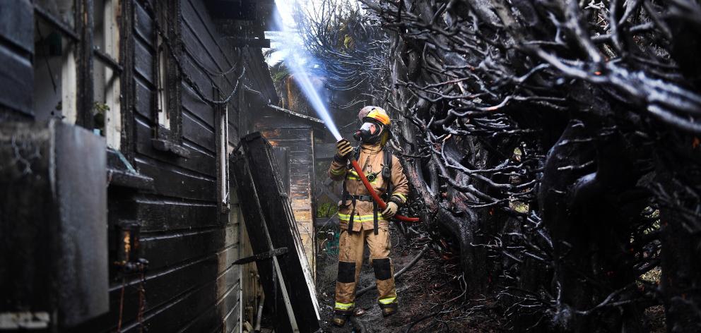 A firefighter dampens down the back wall of a house at Warrington after a burning hedge set fire...