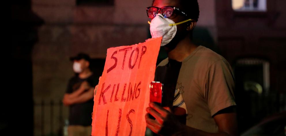 A man wearing a protective face mask holds a sign during a protest in the Brooklyn borough of New...
