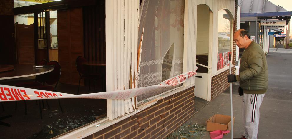 Gin’s Restaurant owner Jimmy Au Yeung cleans up debris after a ute slid on ice and crashed into...