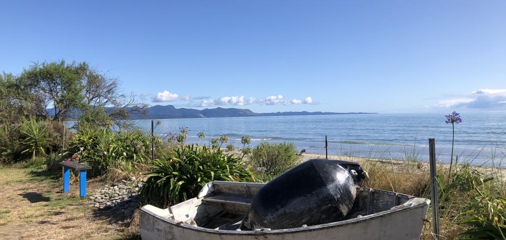 Blue sky, calm sea, and a local dinghy create a picturesque scene at Patons Rock, Golden Bay....