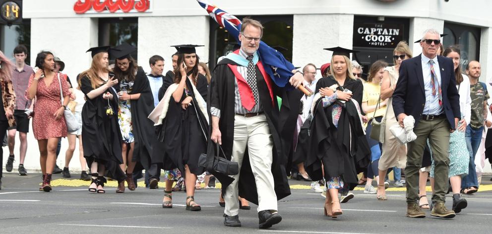 Caroline Freeman College warden Chris Addington, carrying a New Zealand flag, and students and...