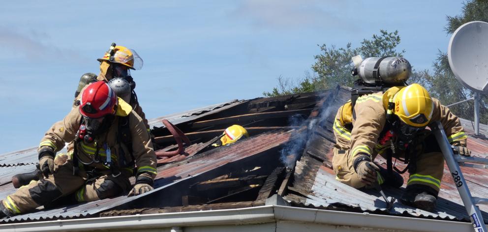 Firefighters lift roofing iron to tackle hot spots at a house fire at the corner of Ventry and...