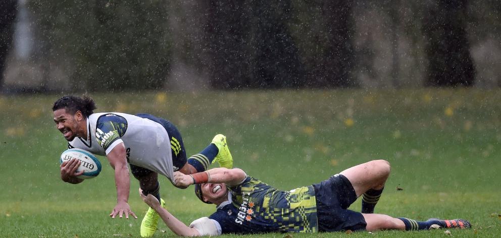 Highlanders halfback Folau Fakatava is tackled by Marty Banks during a wet training session at...