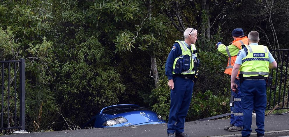 Police inspect the scene where a vehicle crashed down a bank in Pine Hill Rd yesterday. PHOTO:...
