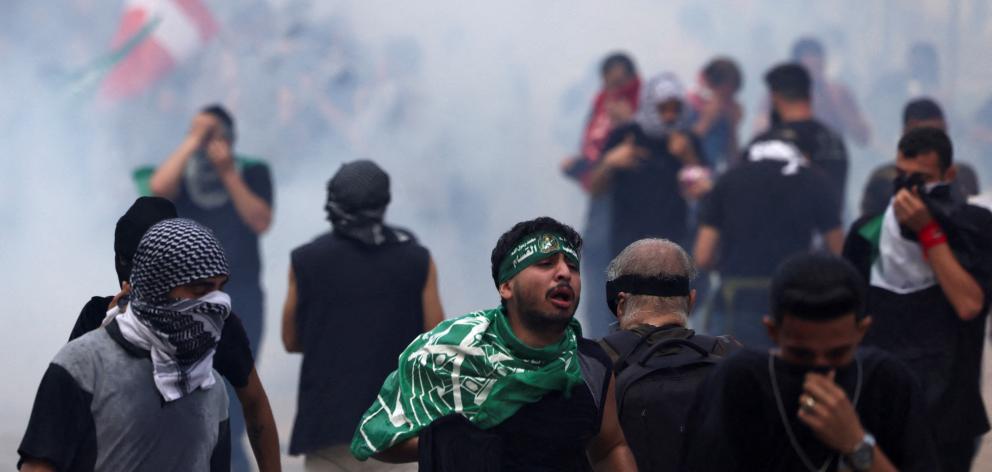 People react among a cloud of tear gas while clashing with security forces during a protest in...