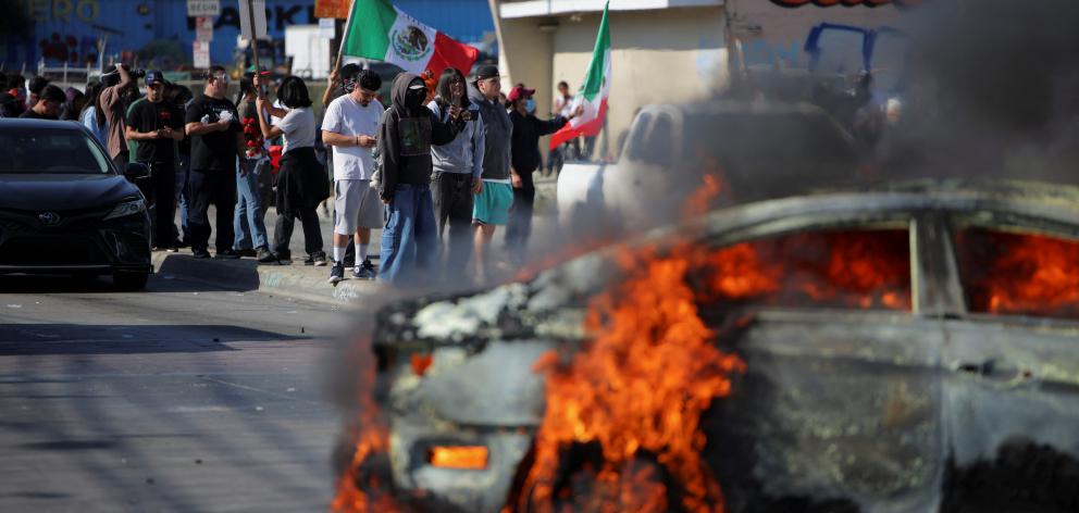 Protesters stand near a burning car following multiple detentions by Immigration and Customs...