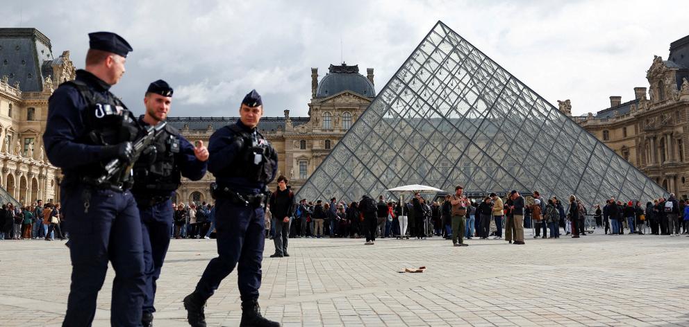 French CRS riot police officers walk near the glass Pyramid of the Louvre Museum, after French...