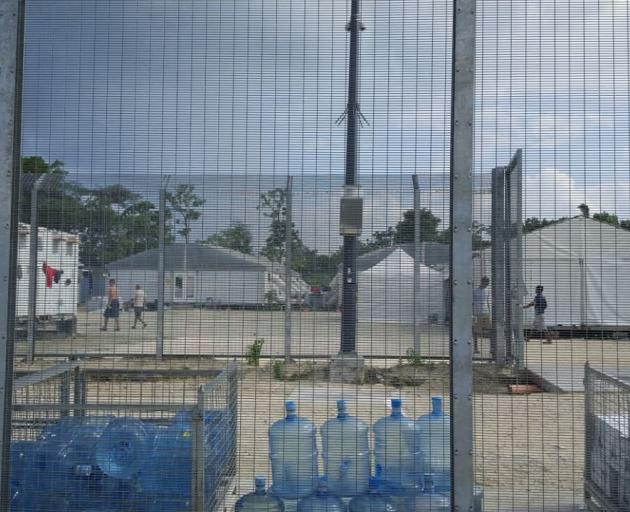 Detainees walk around the compound near a stack of water bottles inside the Manus Island...
