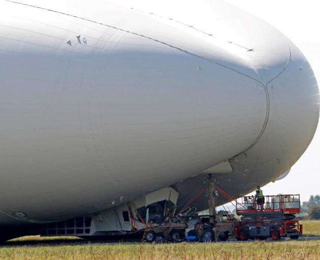 Workers look at damage to the Airlander 10 after the test flight at Cardington Airfield. Photos...