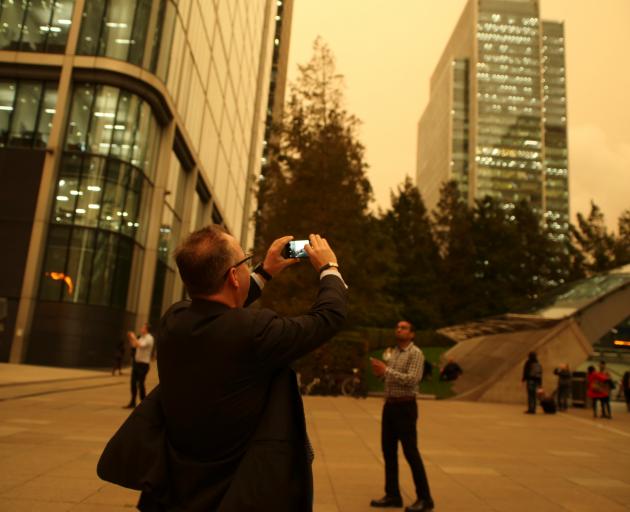 A man photographs the sky turning reddish yellow over buildings in Canary Wharf. Photo: Reuters