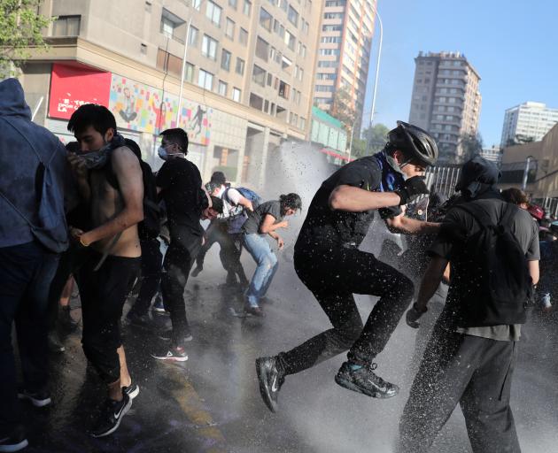 Demonstrators try to avoid water sprayed during a protestin Santiago on Monday. {Photo: Reuters)
