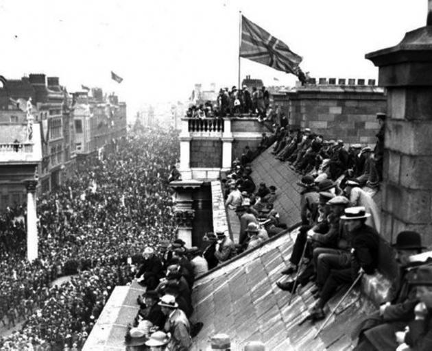 People sit and stand atop Trinity College's West Front building, which is flying the Union Jack,...