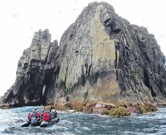 A Heritage Expeditions Zodiac and passengers get up close and personal with one of the sheer...