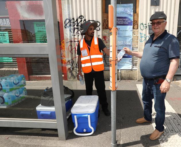A Melbourne transport worker hands out water to a man waiting for a bus as the city bakes under...