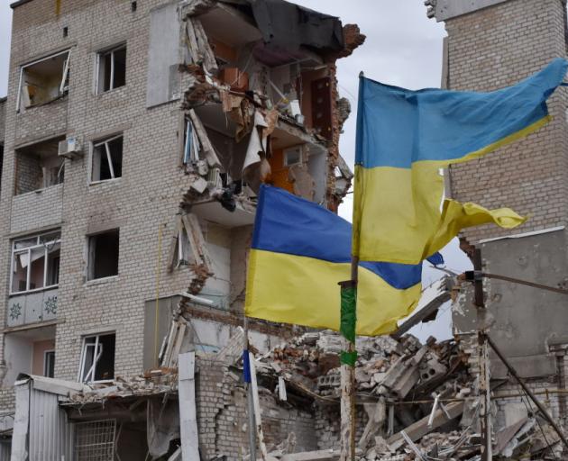 Ragged Ukranian flags flutter in front of an apartment building heavily damaged by Russian...