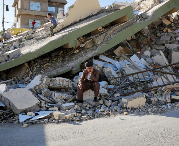 A man sits on a concrete in front the collapsed building at Derbendihan district of Sulaymaniyah in Iraq. Photo: Getty Images