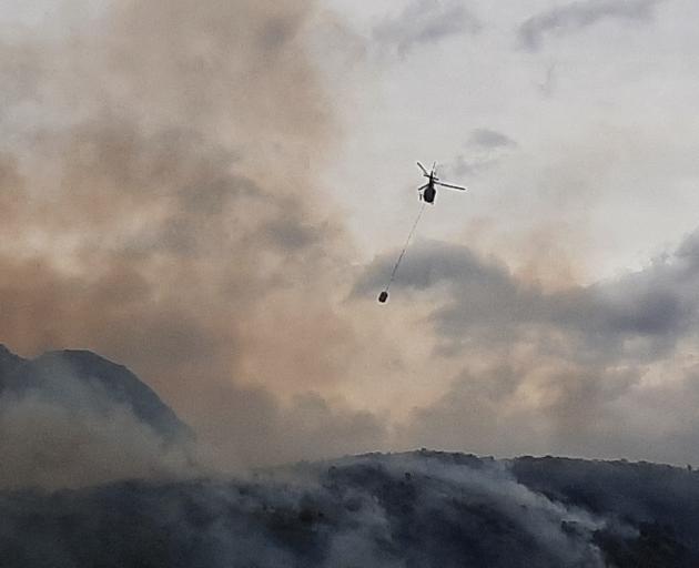A helicopter with a monsoon bucket at the fire above Glendhu Bay, Wanaka. Photo: Kaj Christensen