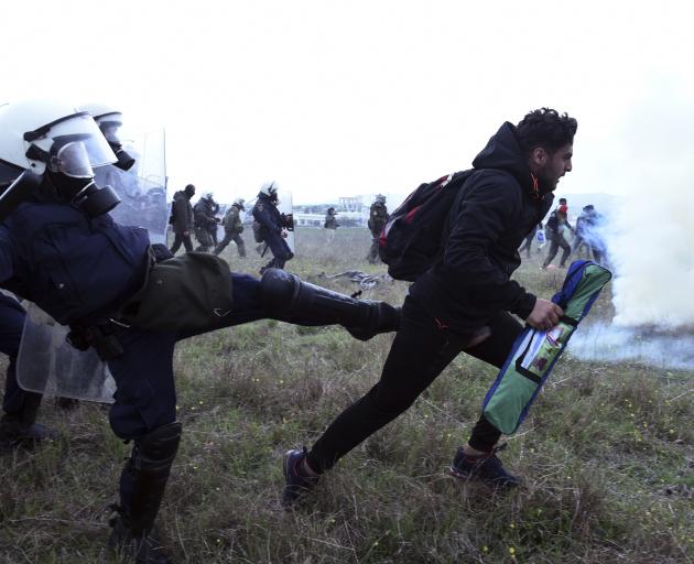 A policeman kicks out at a migrant during clashes outside a refugee camp in the village of...