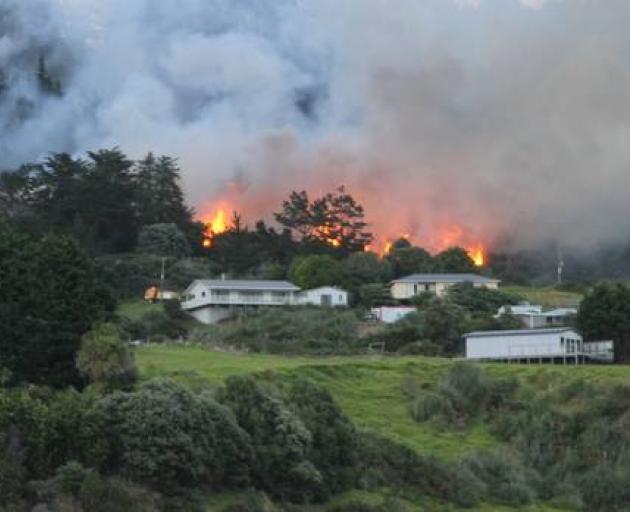 A bush fire flares on the hills above houses at Ahipara. Photo: Northland Age via NZ Herald