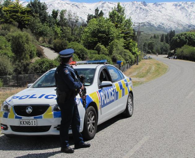 An armed police officer mans a road block on Lowburn Valley Rd, near Cromwell. Photo: Pam Jones