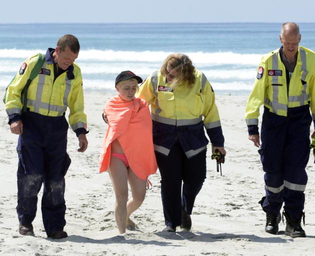 Brighton Fire and Emergency New Zealand volunteers help a woman to an ambulance after she was rescued from the surf at Ocean View yesterday. Photo: Gerard O'Brien