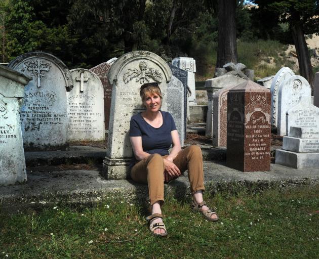 New Kaitangata resident Denise Dent sits in front of headstones at the local cemetery, including those for miners killed on February 21, 1879. Photo: Christine O'Connor