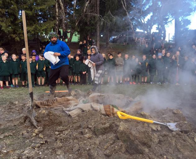 Green Island School pupils watch Manawa En terprises teachers Kopua Waititi and Ana Pene prepare to lift a hangi in the school grounds. Photo: Shawn McAvinue