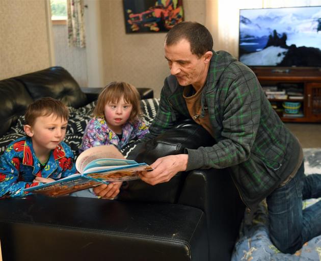Parent Brendan Selwood reads to his children Alex (6) and Emily (8) at their Brighton home, in which they all sleep in the lounge. Photo: Stephen Jaquiery