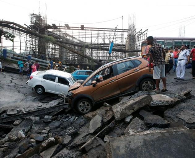 People stand next to the wreckage of vehicles at the site of a bridge that collapsed in Kolkata. Photo: Reuters People stand next to the wreckage of vehicles at the site of a bridge that collapsed in Kolkata. Photo: Reuters
